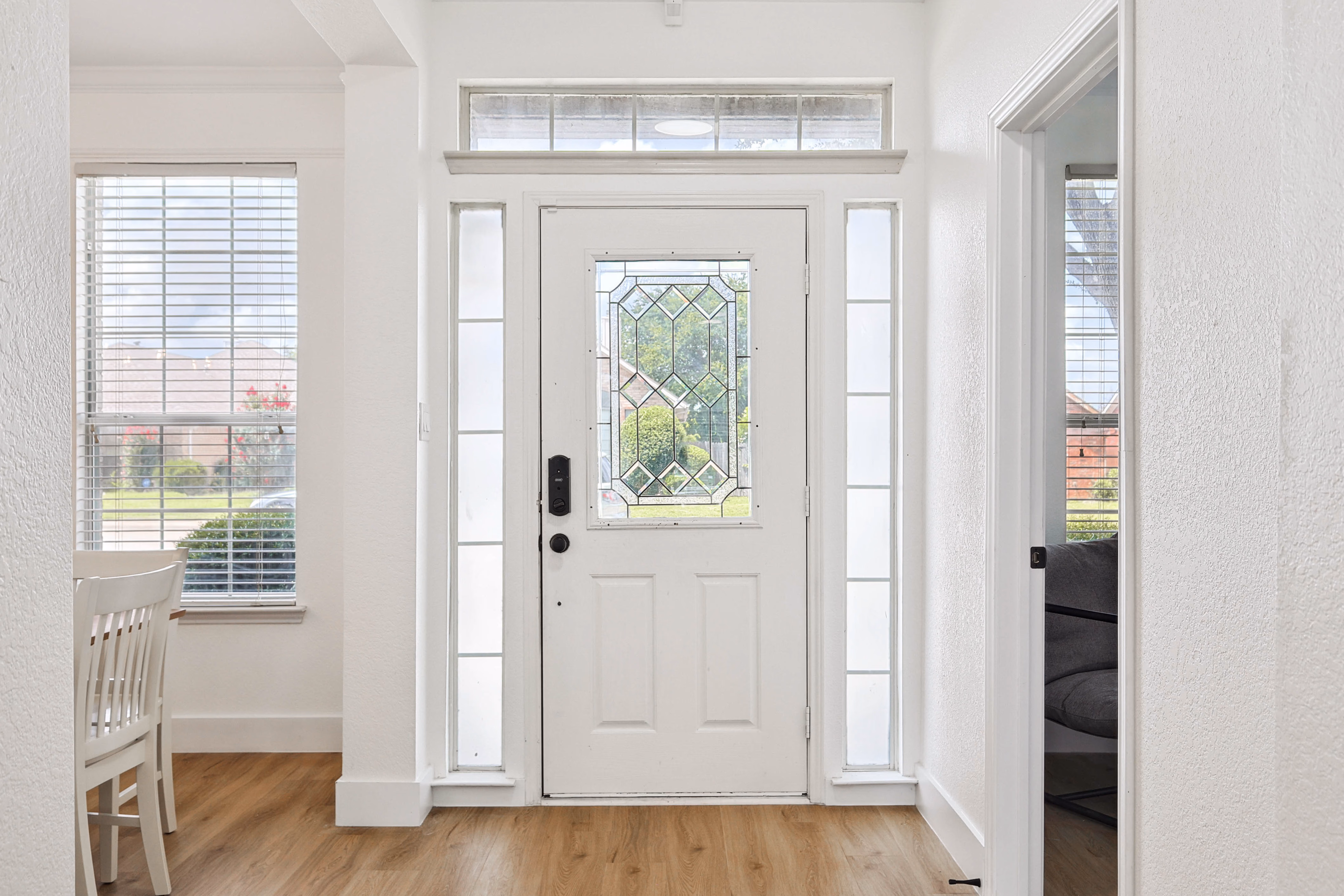 Foyer — leaded-glass front door, smart lock, luxury vinyl floors, sightline into downstairs bedroom.