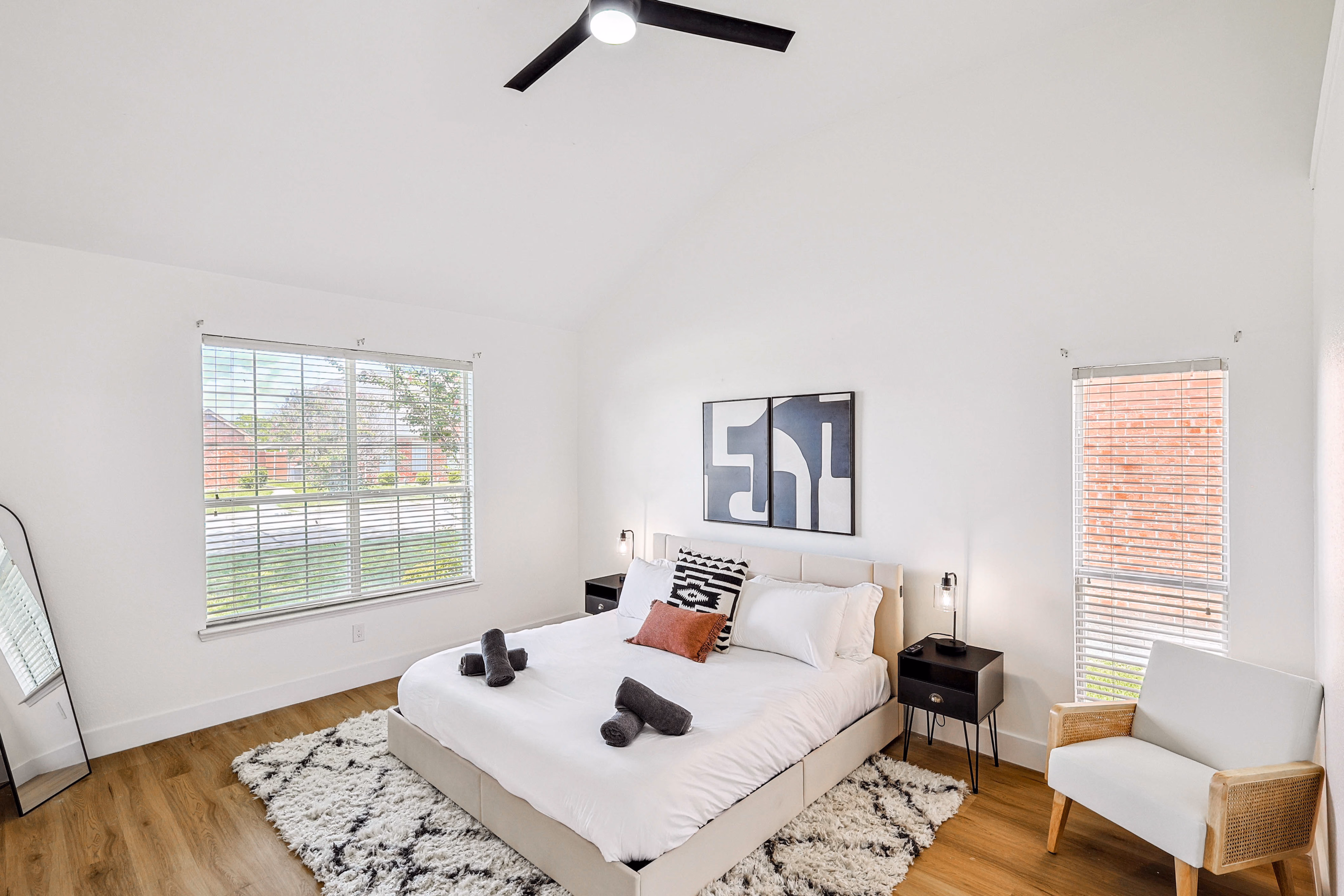 Primary bedroom — king bed with abstract art under vaulted ceiling, two windows, leather chair in corner.