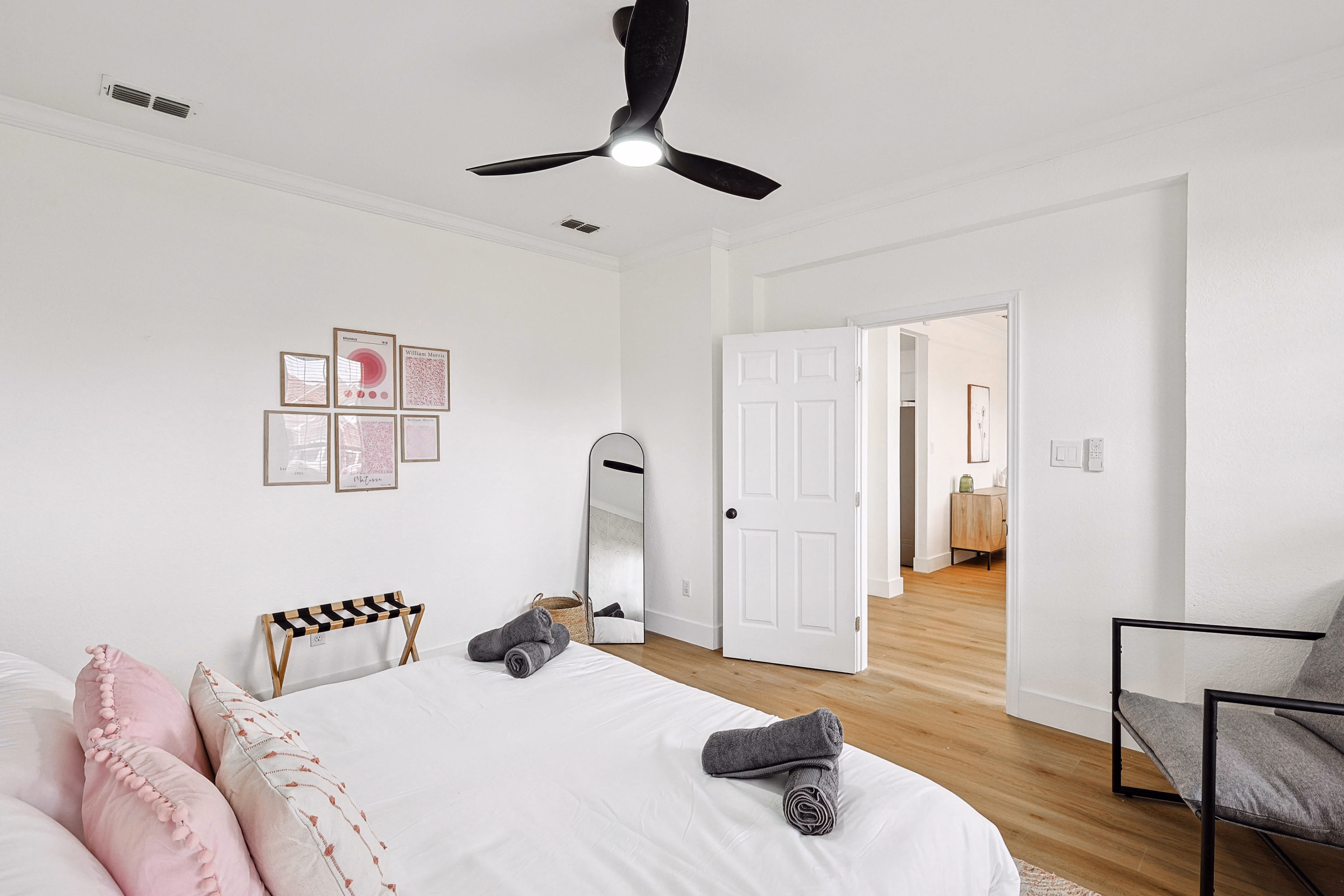 Upstairs bedroom — queen bed with pink microscopy gallery wall, leaning floor mirror, view through doorway toward loft.