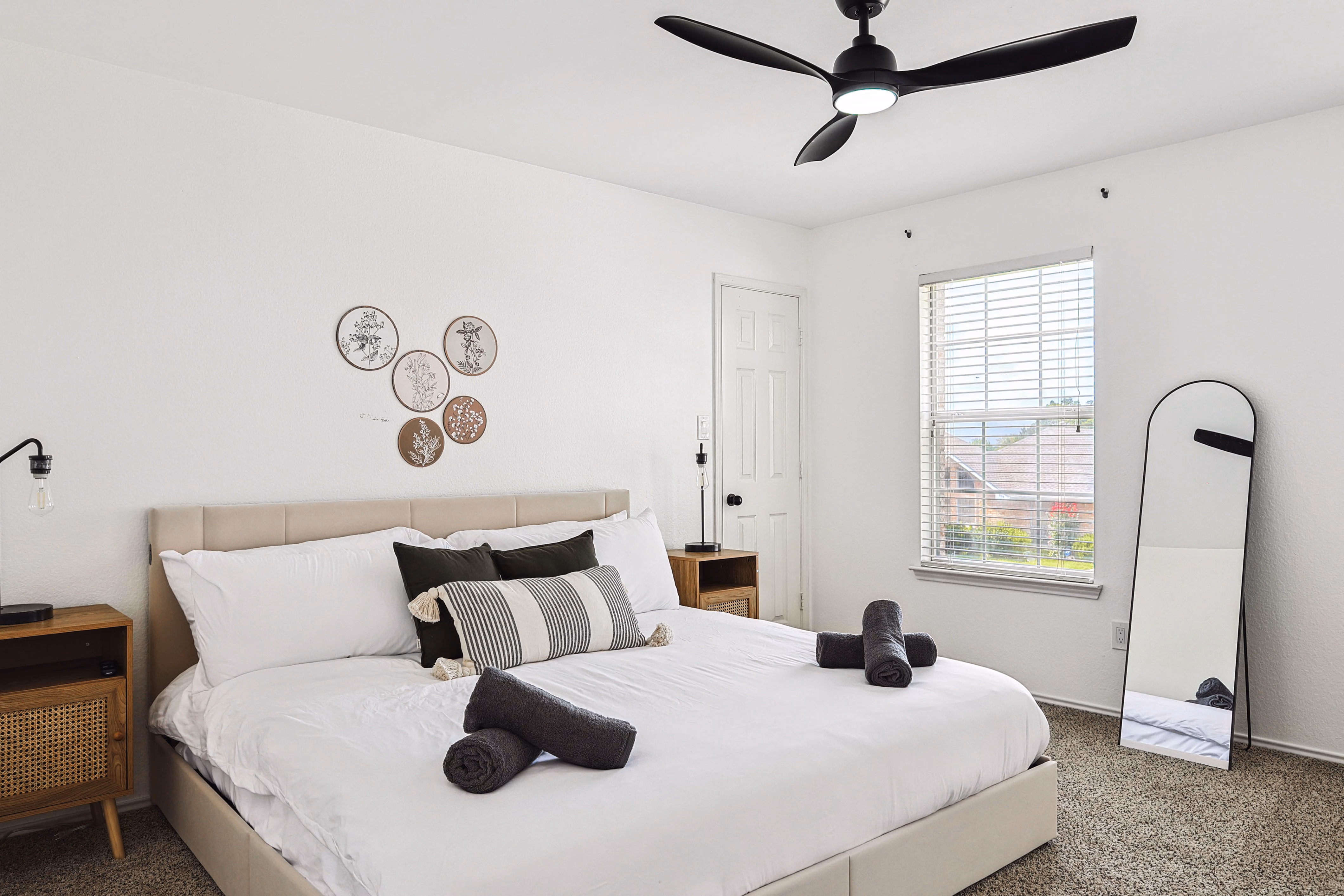 Upstairs bedroom — king bed with botanical-plate wall art, leaning arched mirror, leather accent chair.