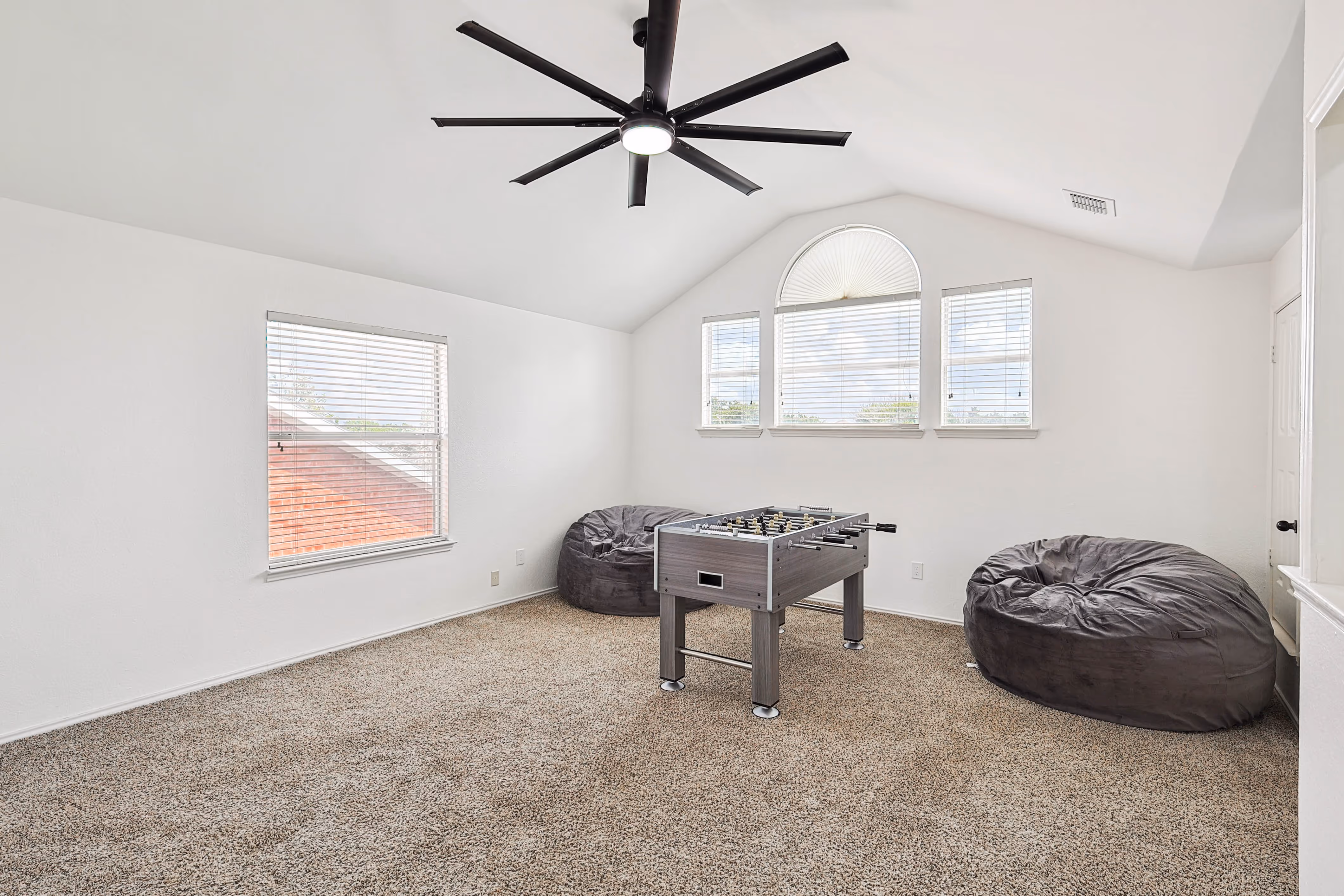 Longleaf — Loft game room — vaulted ceiling, oversized fan, foosball table flanked by oversized bean bags, half-moon arched window.