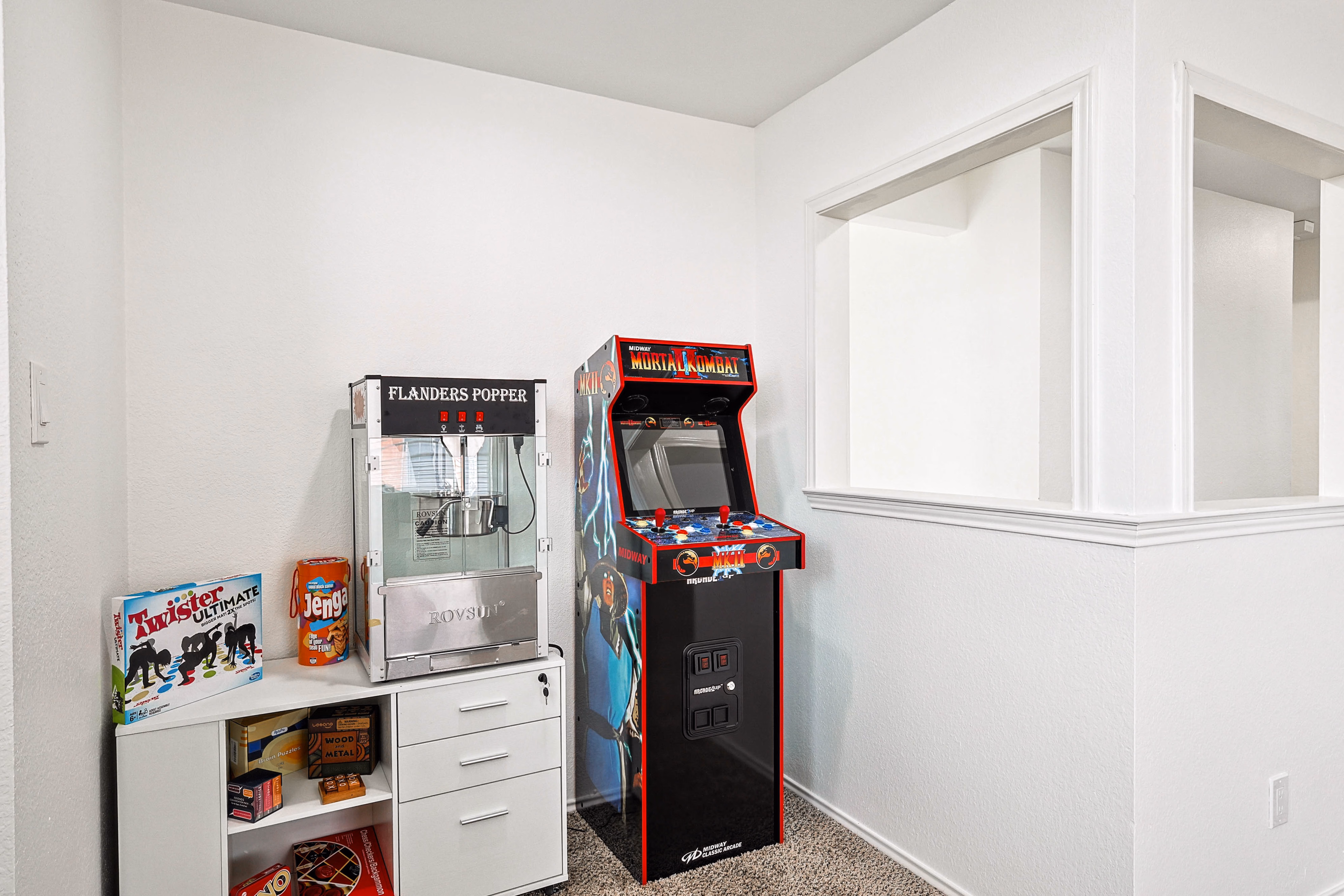 Loft game room — Flanders popcorn machine, Mortal Kombat arcade and shelf of board games beside open railing.